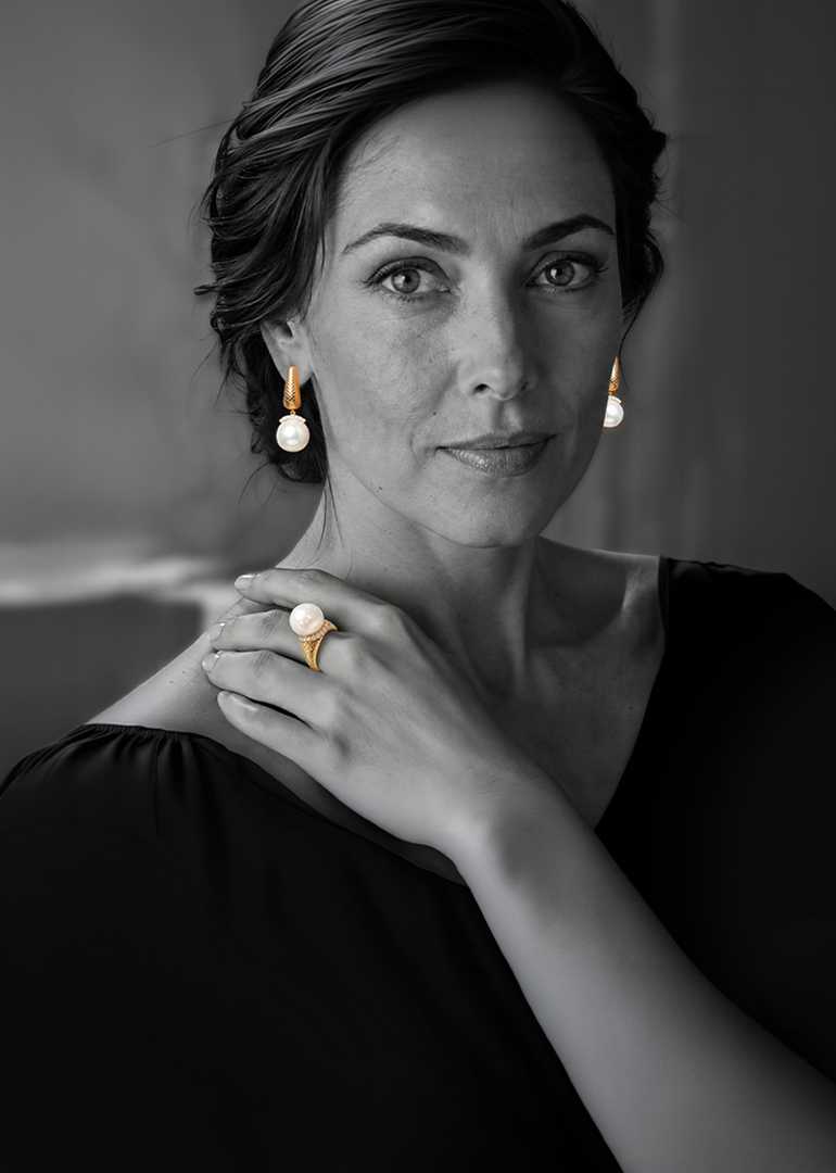 Black-and-white portrait of a woman wearing Colette Falchet Alma Mater South Sea pearl and diamond ring and earrings, with the 18k yellow gold jewelry shown in color. Mobile.