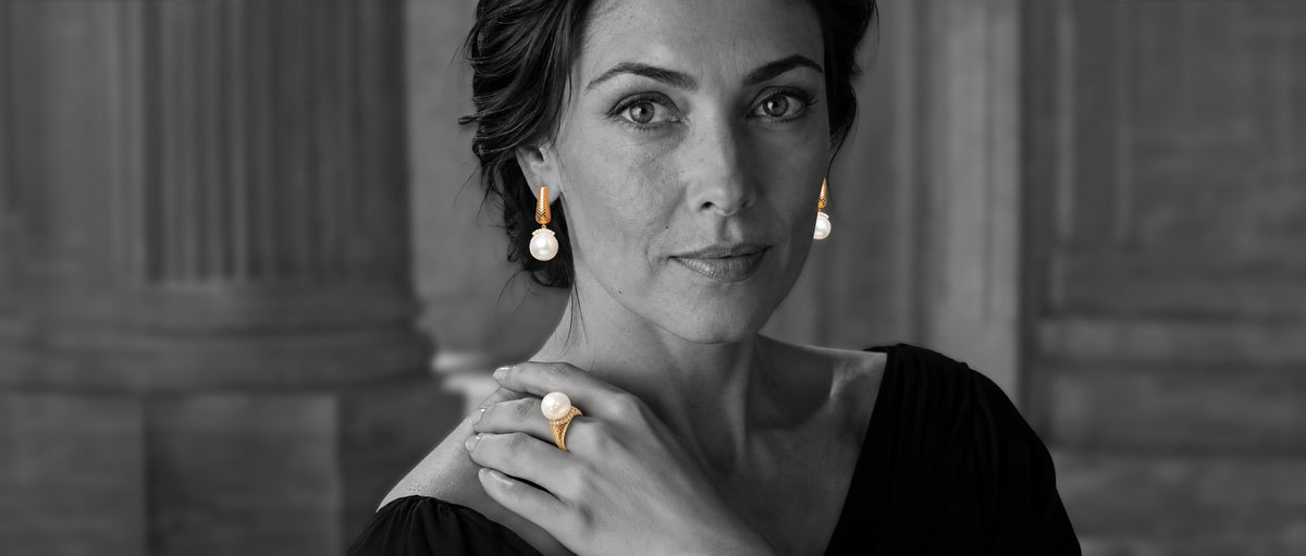 Black-and-white portrait of a woman wearing Colette Falchet Alma Mater South Sea pearl and diamond ring and earrings, with the 18k yellow gold jewelry shown in color.