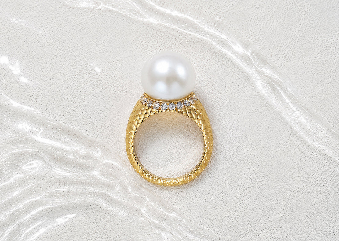 Side view of the Colette Falchet Alma Mater ring in 18k yellow gold, featuring a white South Sea pearl, natural diamonds and a sculpted scale-pattern band.